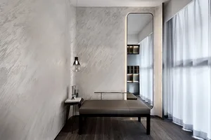 A minimalist living room with concrete walls and a small bench, featuring a modern light fixture and a large mirror.