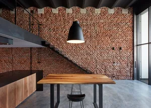 An industrial-style office space featuring a brick wall, a wooden table, concrete floor, and metal stairs.