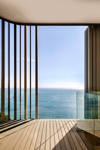 A modern terrace overlooking the ocean, featuring large glass windows and wooden flooring.
