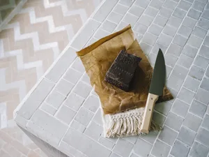 A package of brown paper with a knife and a bar of chocolate, placed on a textured fabric.