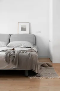 A modern bedroom featuring a grey upholstered bed with white bedding and a grey textured throw blanket.