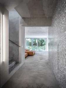 A spacious modern living room featuring concrete walls and flooring, with a large window overlooking a garden.