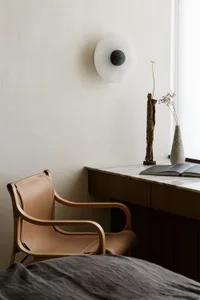 Modern interior featuring minimalist design with wooden furniture, a round wall lamp, and a table with a book and vase.