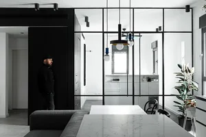 A modern dining room featuring glass walls, white cabinets, marble countertops, and black furniture.