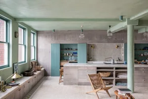 A modern kitchen with concrete walls, wooden cabinets, and a large island.