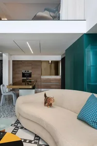 A modern living room featuring a beige curved sofa, blue patterned rug, and a green wall.