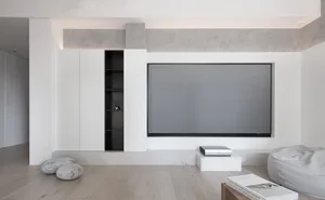 Modern living room with a large flat-screen TV, minimalist furniture, and a concrete fireplace.
