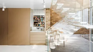 A sleek, modern office space featuring glass, metal, and concrete materials, with a glass-enclosed staircase and bookshelves.