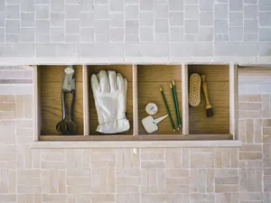 A wooden drawer with compartments containing various tools and items such as scissors, gloves, pencils, and brushes.