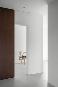 A minimalist interior space featuring concrete walls and floors, with a single wooden chair.