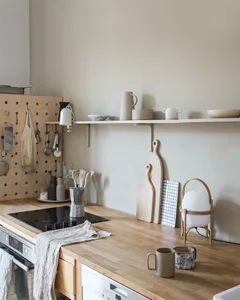 A minimalist kitchen with a wooden countertop, hanging utensils, and various mugs and bowls on a shelf.