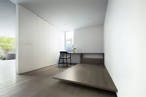 Modern minimalist home office with a counter desk made of wood, featuring a chair and a lamp.