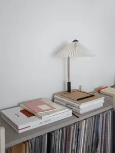 A minimalist shelf made of wood with books, a frame, and a table lamp.