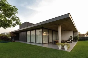 Modern residential house featuring glass windows, concrete pillars, metal roofing, and potted plants.