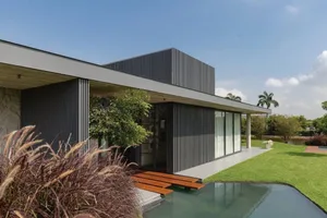 Contemporary house with metal cladding and glass doors on a sunny day, featuring a pool and landscaped garden.