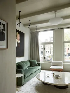 Contemporary living room in minimalist design with a green sofa, round glass coffee table, and large windows.