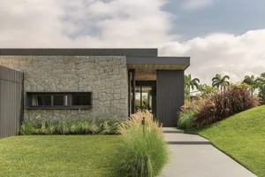 A modern residential exterior featuring sandstone walls and a metal roof.