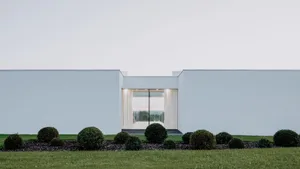 Modern residential exterior with minimalist design featuring white stucco walls and large glass window.