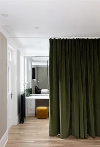 Modern bedroom with green velvet curtain, white walls, hardwood floor, and black radiator.