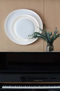 Ceramic plates arranged on the wall with greenery in a vase on top of a black Yamaha piano.