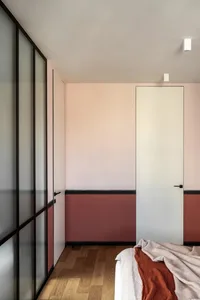 A minimalist bedroom with wooden floors, glass doors, and a red blanket on the bed.