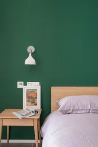 A minimalist bedroom with a wooden headboard on a green wall, featuring a bed with white bedding and a side table with a fram