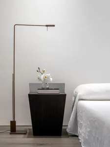 A minimalist bedroom with a wooden side table featuring a vase of white flowers and a book.
