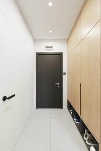 A minimalist entrance way featuring a black door, light wood cabinetry, and a laminate floor.