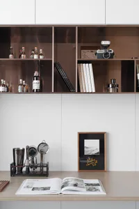 A modern minimalist home bar with wooden shelves filled with bottles, books, and a camera, along with a wooden frame and a ma