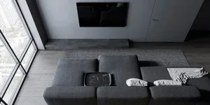 Modern minimalist living room with dark gray sofa, marble coffee table, and large windows overlooking the city.