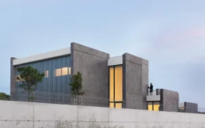 Modern, minimalist house exterior showcasing sleek, concrete finishes and large glass windows.