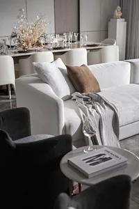 A modern living room with a white sofa, grey armchairs, and a dining table set with glasses and plates.
