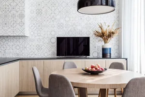 A modern minimalist kitchen with a round wooden table, chairs, and a flat-screen TV on the wall.