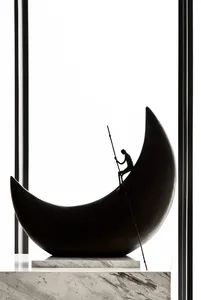 A metal crescent moon sculpture featuring a figure climbing it with a staff, positioned indoors.