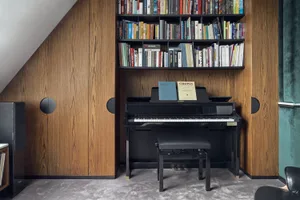A minimalist music room featuring wooden shelves filled with books and a black piano with a music stand.