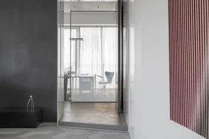 A minimalist office interior featuring glass walls and concrete flooring, with a single chair and desk.