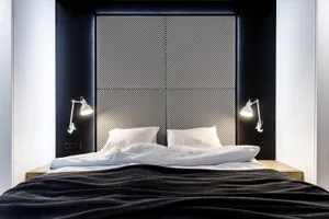 A modern minimalist bedroom with a textured fabric headboard and nightstands with white lamps.