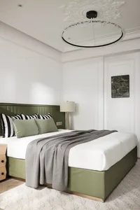A minimalist bedroom with a green leather headboard, grey quilt, and white bedding, decorated with a black and white striped