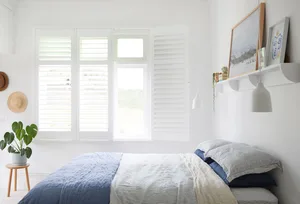 Bedroom with white shutters, blue and white bedding, and a potted plant.