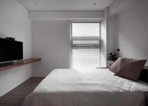 A minimalist bedroom featuring wooden furniture and a bed with a white sheet and a brown pillow.