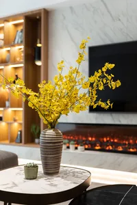 A modern living room with a marble accent wall, fireplace, and a vase of yellow flowers on a round table.