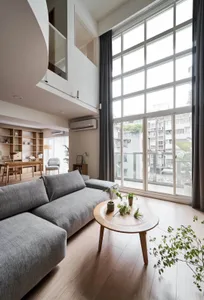 A modern minimalist living room with a comfortable sofa, a round wooden coffee table, and large windows that let in natural l
