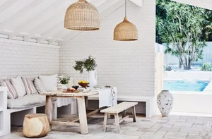 Modern outdoor patio area with wooden furniture, canvas hanging lights, and a concrete pool surrounded by greenery.