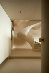 Modern, minimalist interior with a taupe-colored curved staircase and concrete structure.
