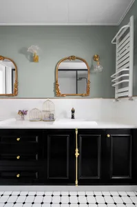 Modern bathroom interior featuring white marble countertop with black cabinets, gold accents, and decorative mirrors.