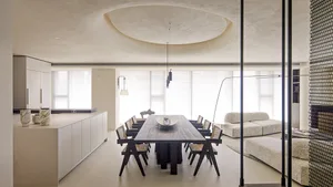 A modern dining room featuring a large marble dining table surrounded by black chairs, set against a minimalist backdrop with