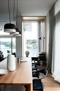 A modern dining room with a view of the water, featuring wooden furniture and minimalist decorative elements.