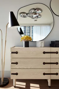Modern dresser with wooden drawers and a round mirror above, featuring decorative ornaments and a potted plant.