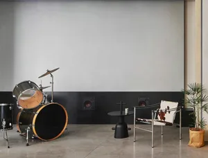 A modern music room featuring a black drum set, a chair with a cowhide cushion, and a plant in a paper bag.