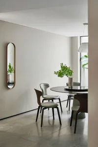 A modern, minimalist dining area with a round table, metal chairs, and a metal mirror.